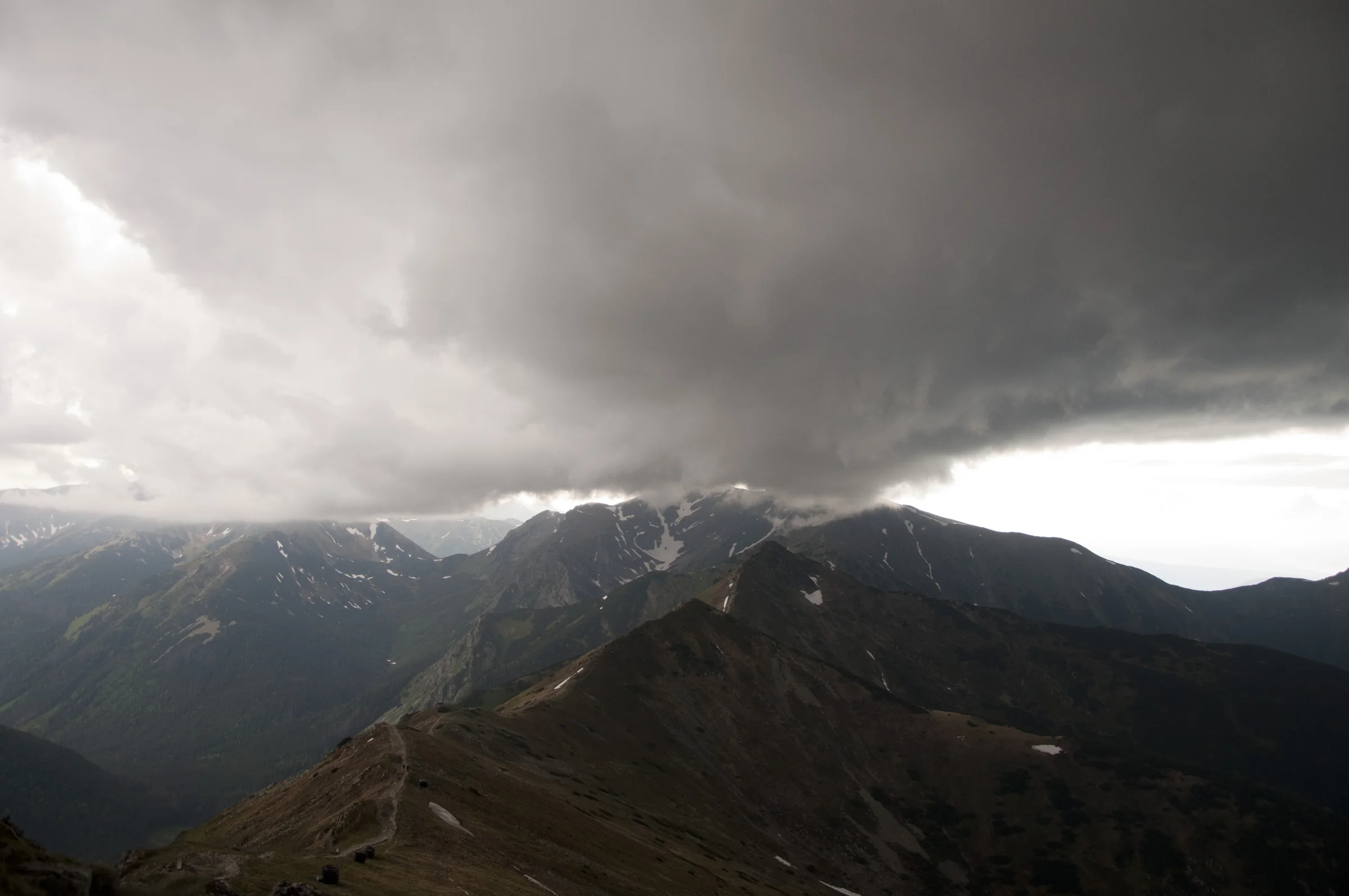 A mountain ridge with patches of snow beneath a low bank of dark storm clouds